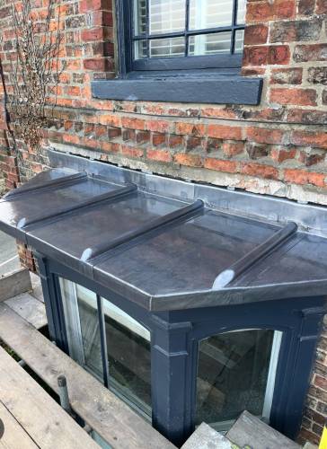 Lead-covered bay roof above a basement entrance on a period brick property